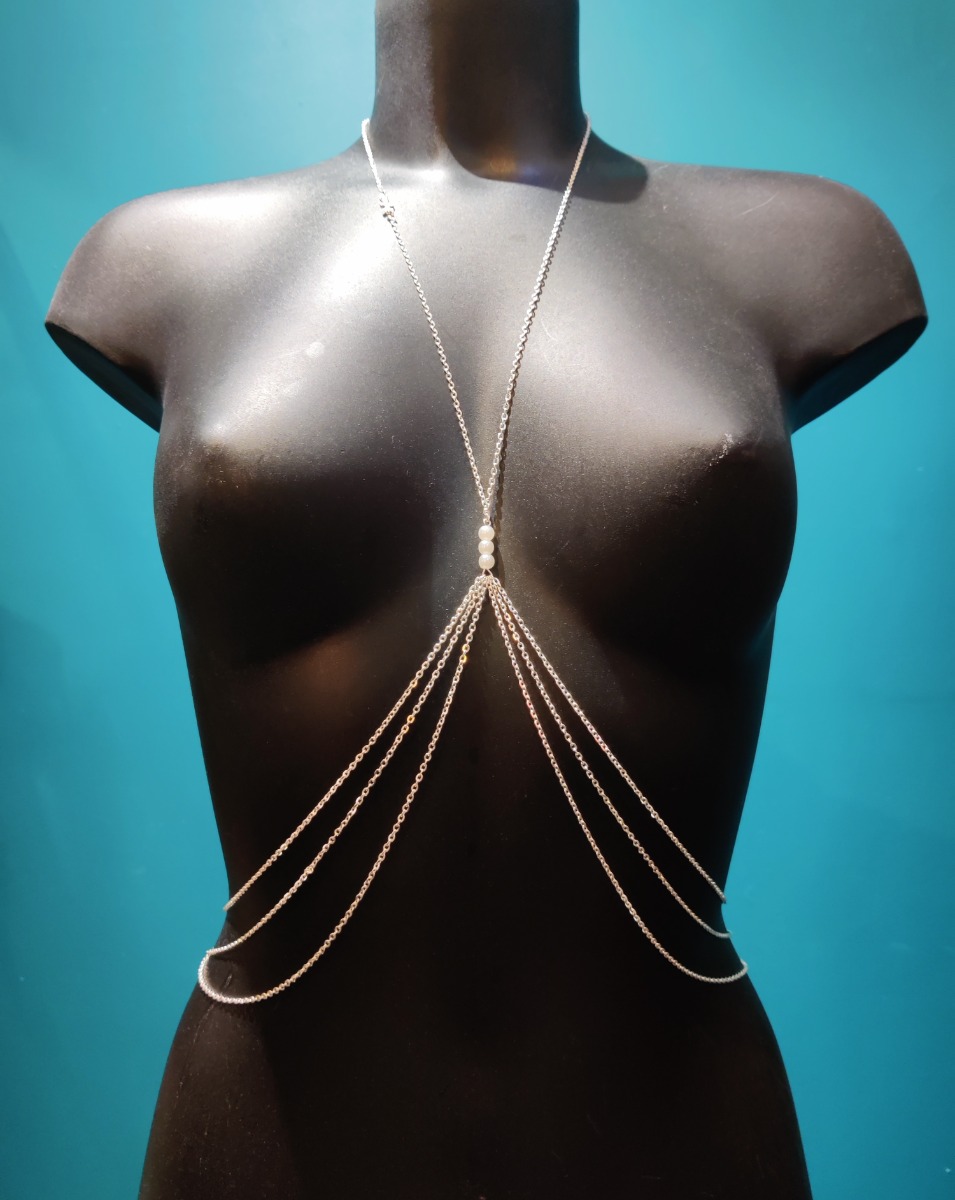 Bijou de poitrine en chaîne fine argentée avec perles blanches sur l&#039;entre-seins et croix sur le collier. 