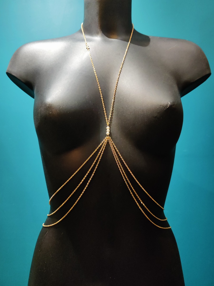 Bijou de poitrine en chaîne fine dorée avec perles blanches sur l&#039;entre-seins et croix sur le collier. 