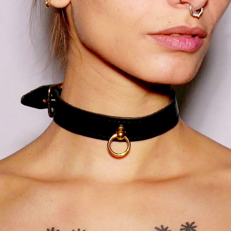 Choker fin en cuir noir surmonté d&#039;un anneau en acier doré. Il se porte comme bijou ou accessoire de jeu de soumission