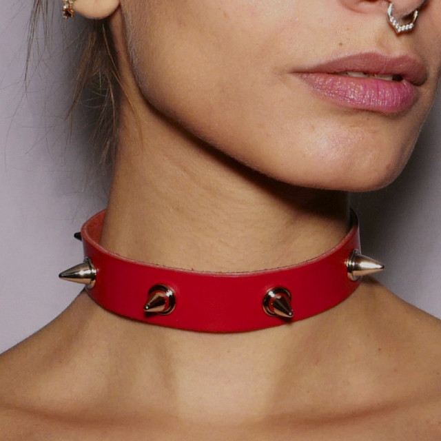 Collier ras-le-cou en cuir rouge orné de pics en acier argenté. Il habille le cou dans un esprit fetish.