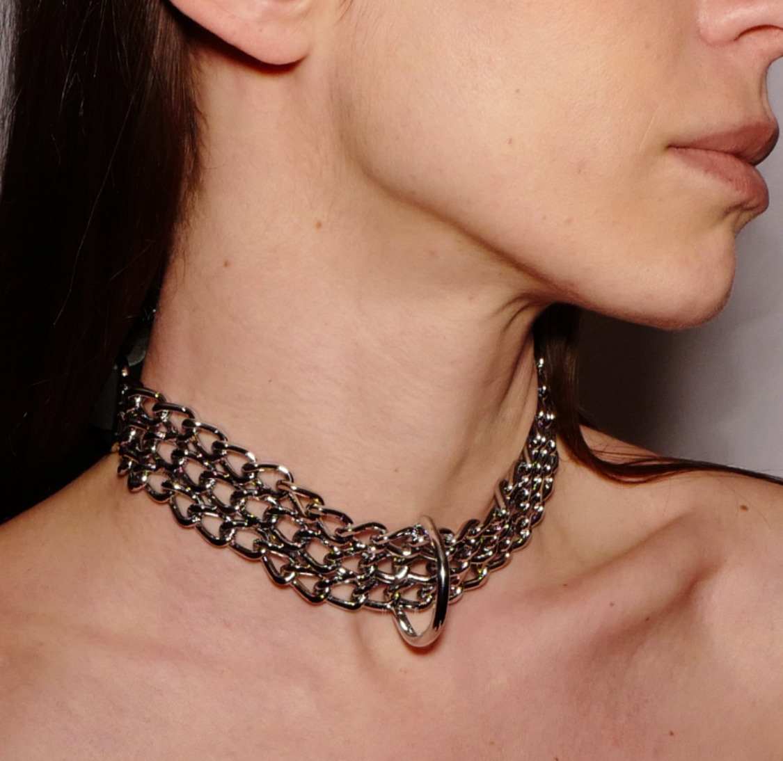 Choker large en chaînes argentées fermé sur la nuque par une bande de cuir noir. Taille unique et réglable en tour de cou
